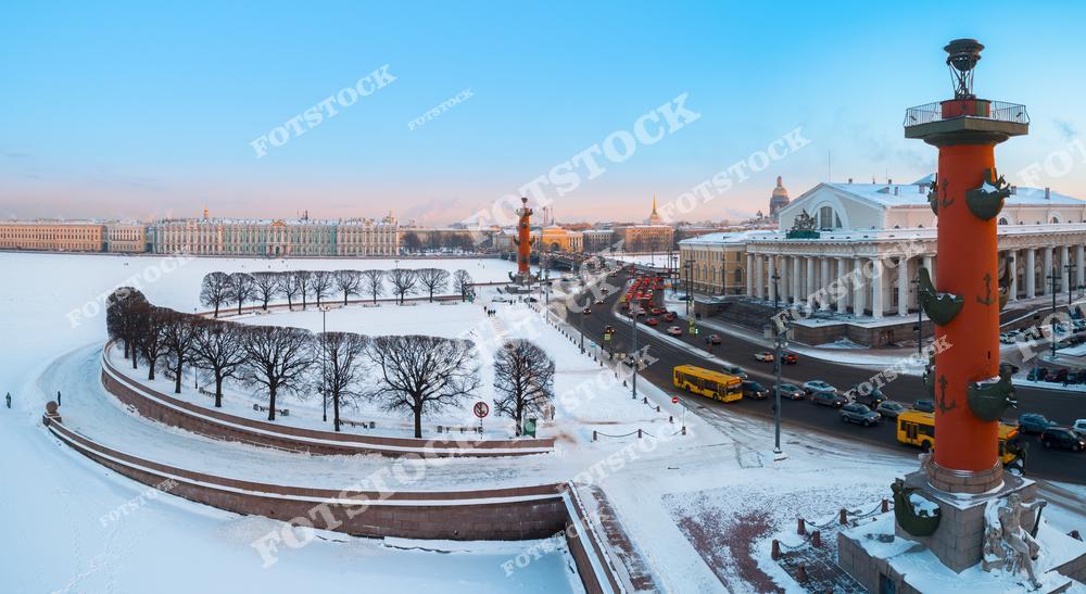 Фотография зимней панорамы Санкт-Петербург, Россия. На изображении запечатлён зимний уличный пейзаж и архитектурный ансамбль Стрелка Васильевского острова с знаменитыми Ростральные колонны на фоне реки Нева. Фотоснимок передаёт атмосферу зимнего Петербурга: холодный свет, простор набережных и величественную архитектуру исторического центра. Фото подчёркивает уникальный облик Санкт-Петербурга как одного из самых узнаваемых городов России. Иллюстрация может использоваться как изображение, картинка или слайд, посвящённые архитектуре и зимним панорамам российских городов.